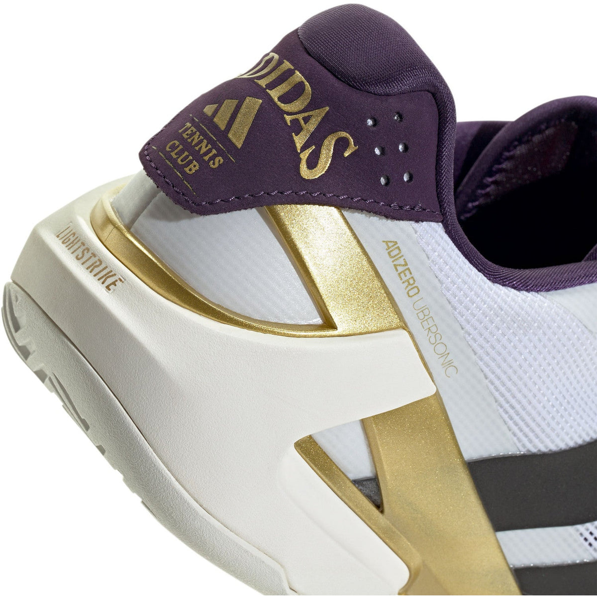 Detalj av den mörklila hälen med guldtryck av ”Adidas Tennis Club” och Lightstrike-mellansula
