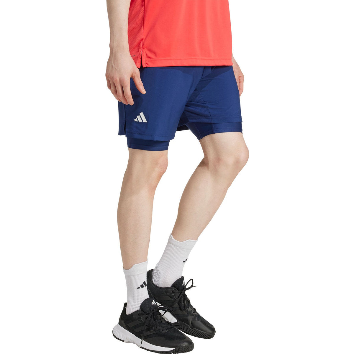 Vooraanzicht van model in de donkerblauwe Adidas Club 2IN1 short met rood sportshirt