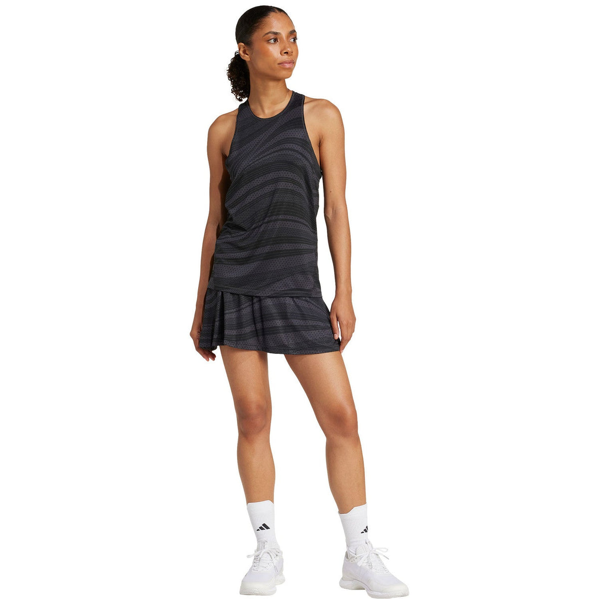 Model in volledige outfit met de donkergrijze Adidas Club Graphic Tank en plooirok