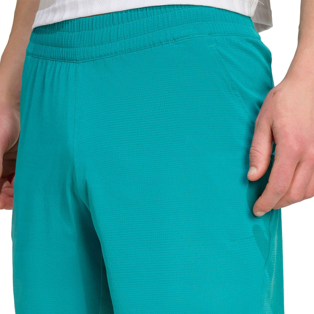 Model stopt een hand in de zijzak van de turquoise Adidas Ergo short