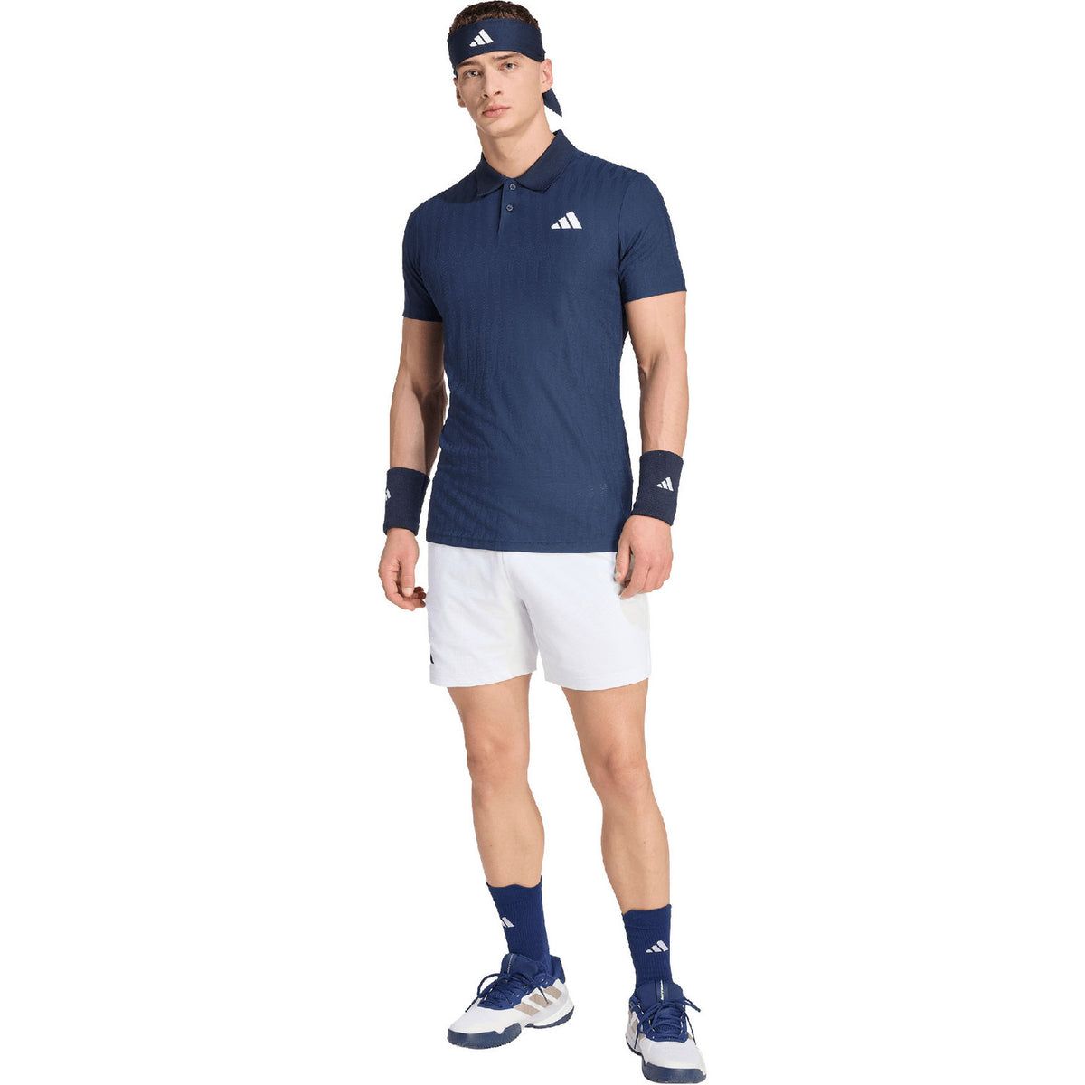 Model met pet draagt de donkerblauwe Adidas Freelift polo en witte short