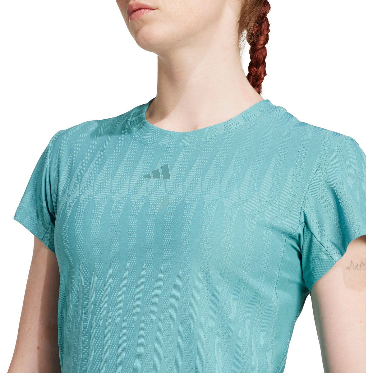 Detail van het logo en de gebreide structuur van het turquoise T-shirt