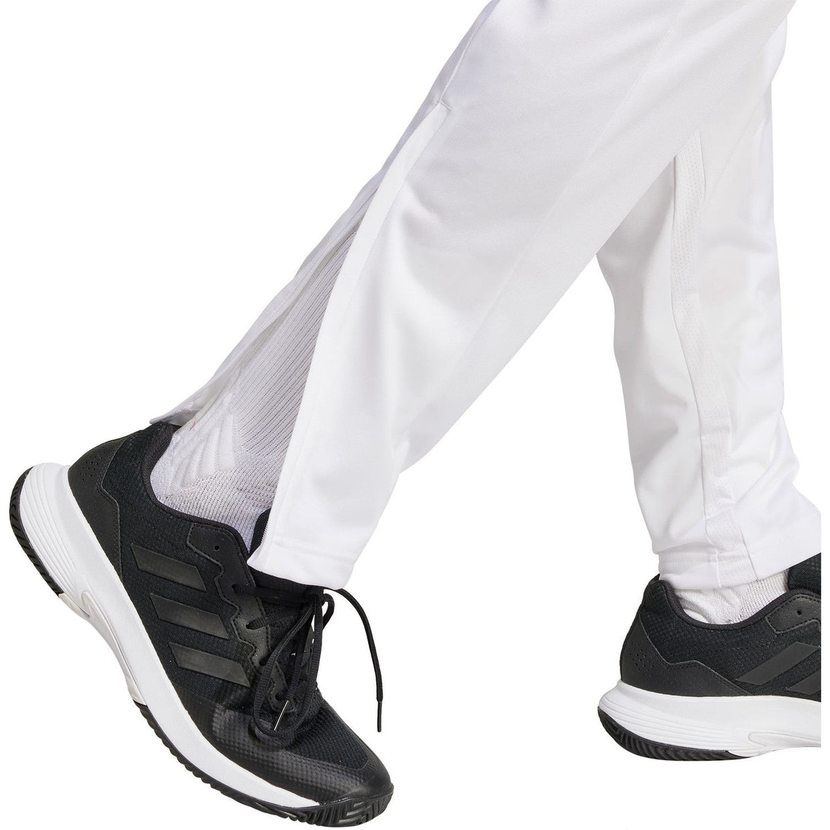 Detail van de enkel van de witte Adidas 3-Stripes broek boven zwarte schoenen
