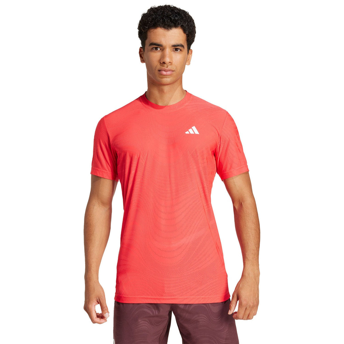 Vooraanzicht van model in het koraalrode Adidas Freelift Pro T-shirt en bordeaux short