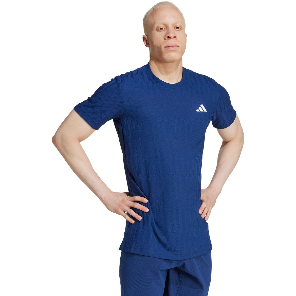 Model draagt het kobaltblauwe Adidas Freelift T-shirt met handen in de zij