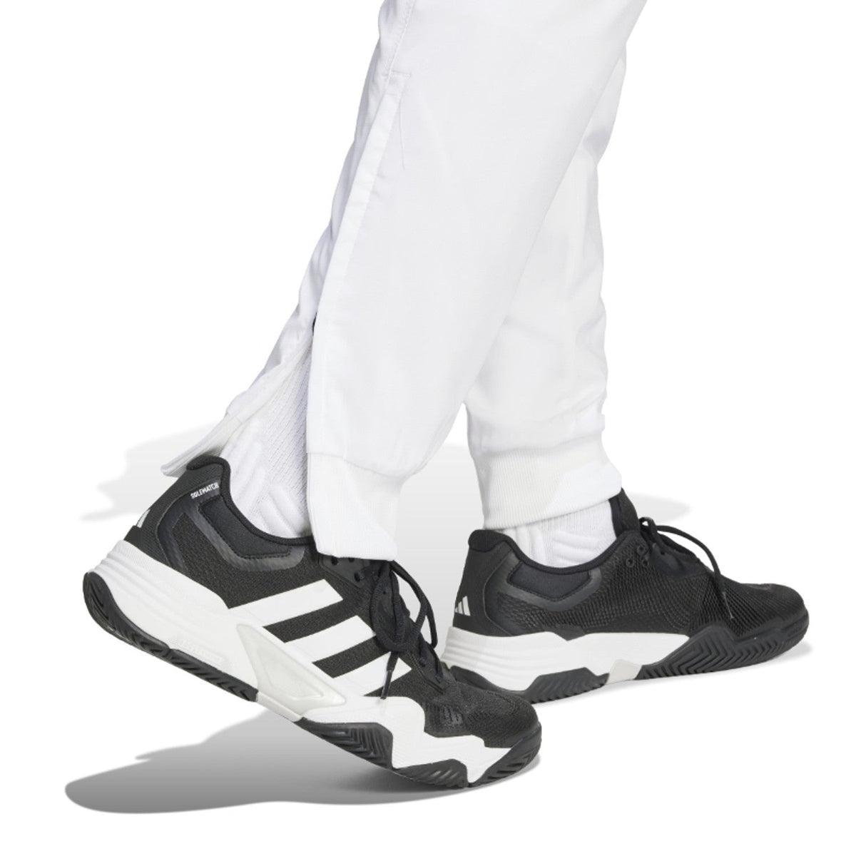 Detail van de enkelboorden van de witte Adidas Walk On broek boven zwarte Adidas sneakers