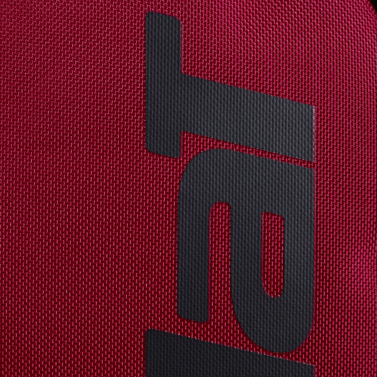 Close-up van het zwarte Babolat logo op de rode stof van de rugzak