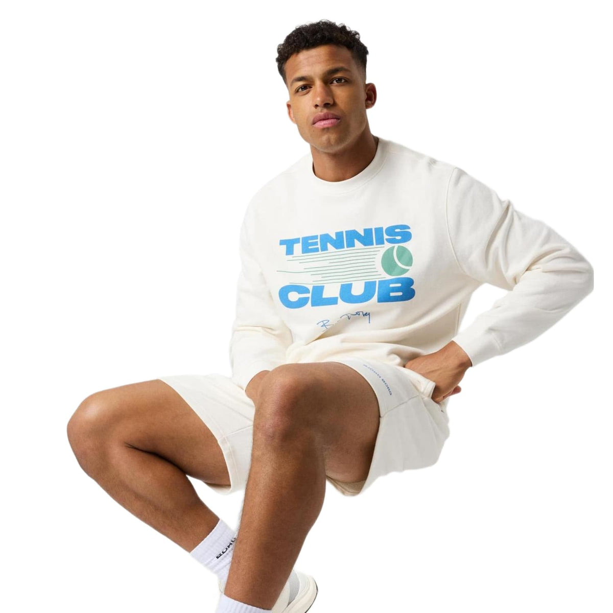 Model zit met opgetrokken been in het gebroken witte Bjorn Borg Tennis Club sweatshirt