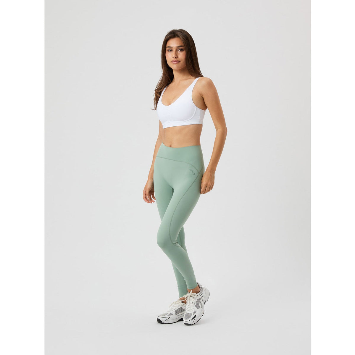 Zijaanzicht ten voeten uit van de witte Bjorn Borg Reform sport-bh met saliegroene legging