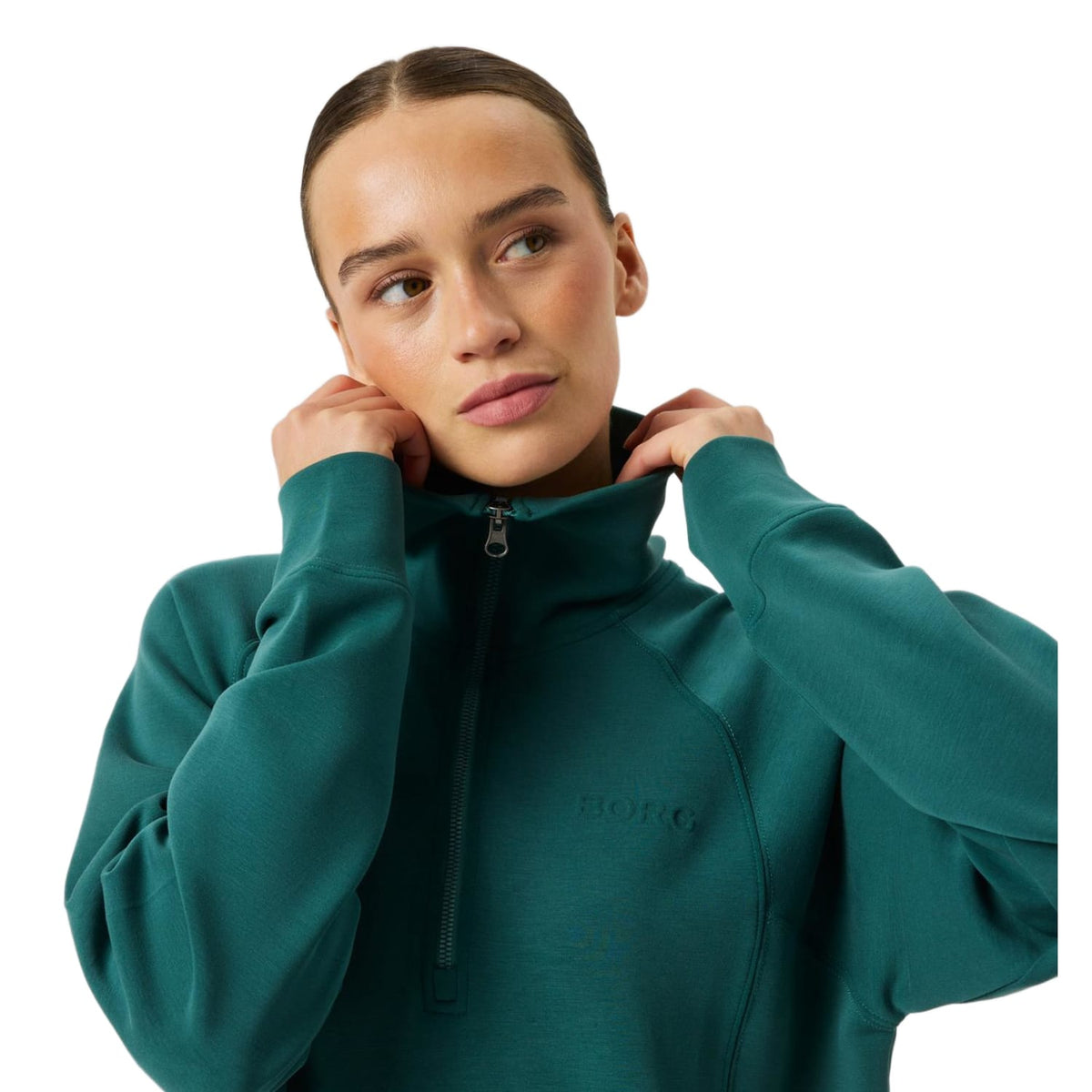 Model trekt de kraag omhoog van de groene Bjorn Borg Studio Soft Halfzip sweater