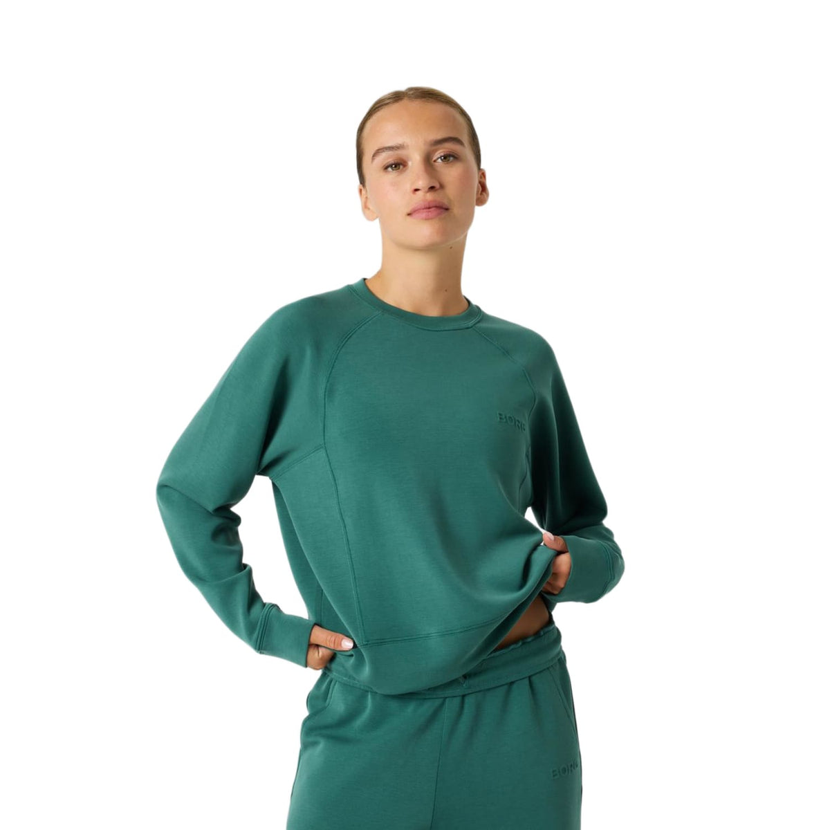 Model draagt de groene Bjorn Borg Studio Soft sweater met de handen in de zij