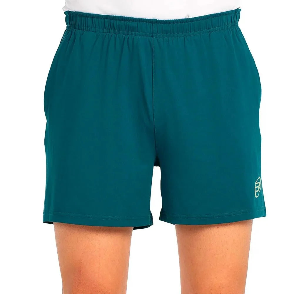 Vue de face du short Bullpadel « Lijar » vert pétrole, avec un logo jaune sur la jambe droite