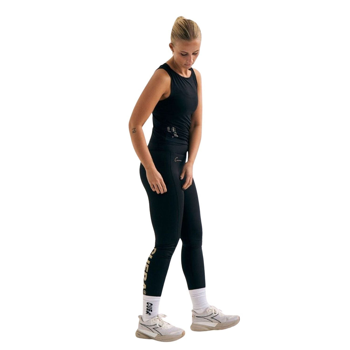Model draagt de Cuera Active Logo Tights Long Black met zwarte tanktop en witte sneakers