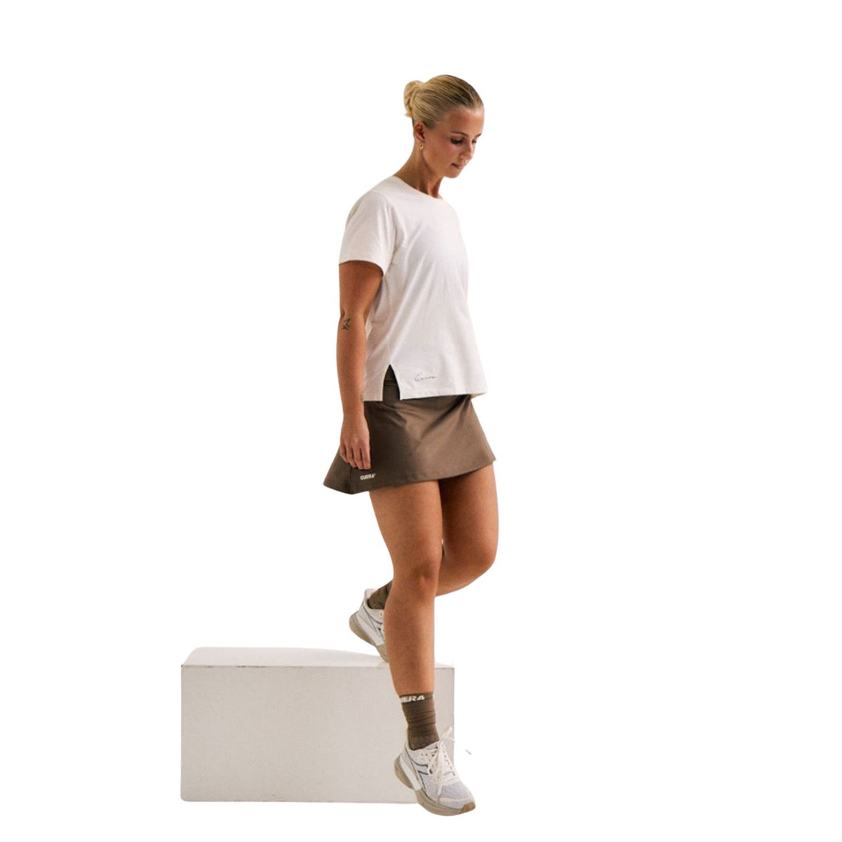 Model draagt de bruine Cuera Oncourt Skirt 2-In-1 met wit shirt en witte padelschoenen