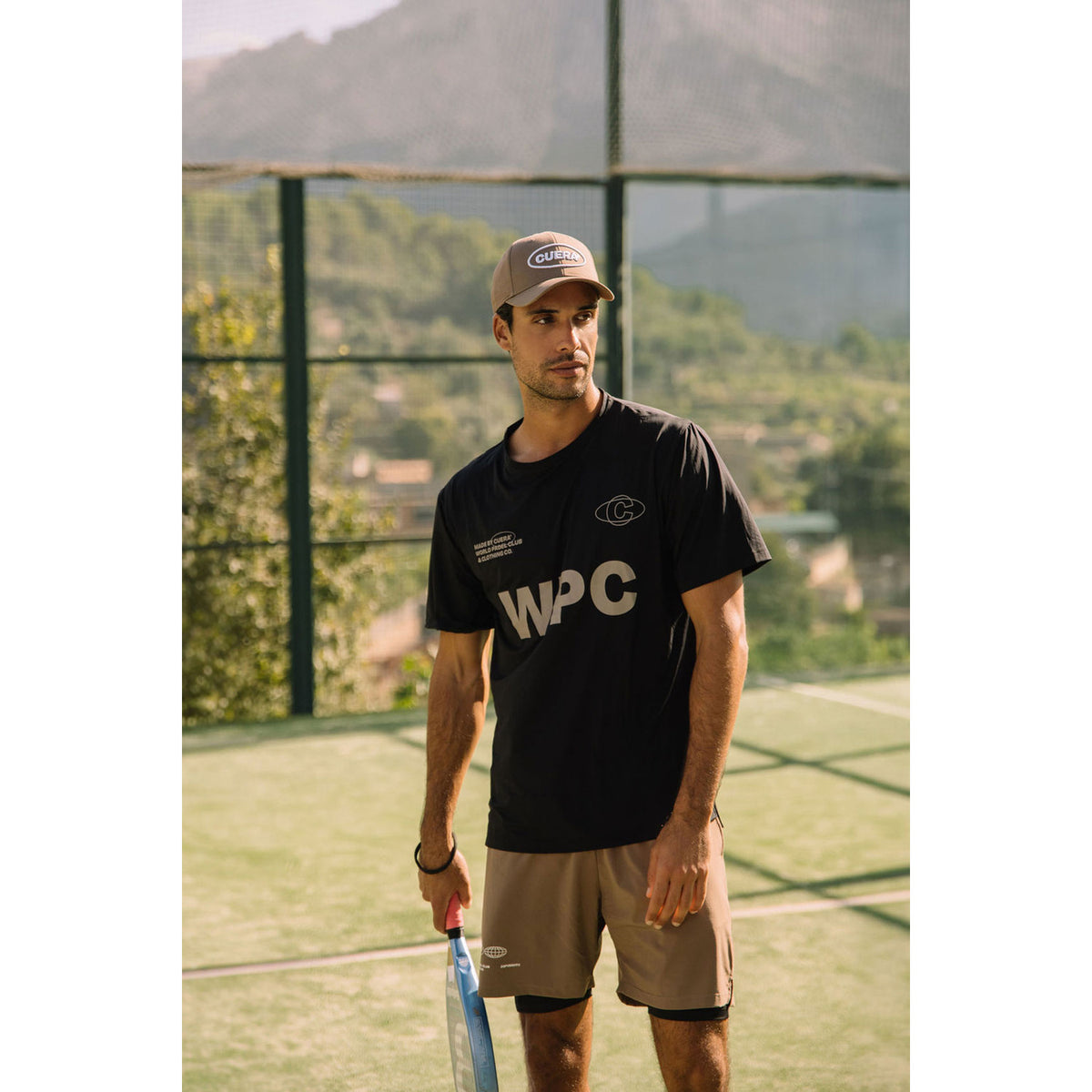 Padelspeler draagt het zwarte Cuera WPC T-shirt met pet en racket op de baan