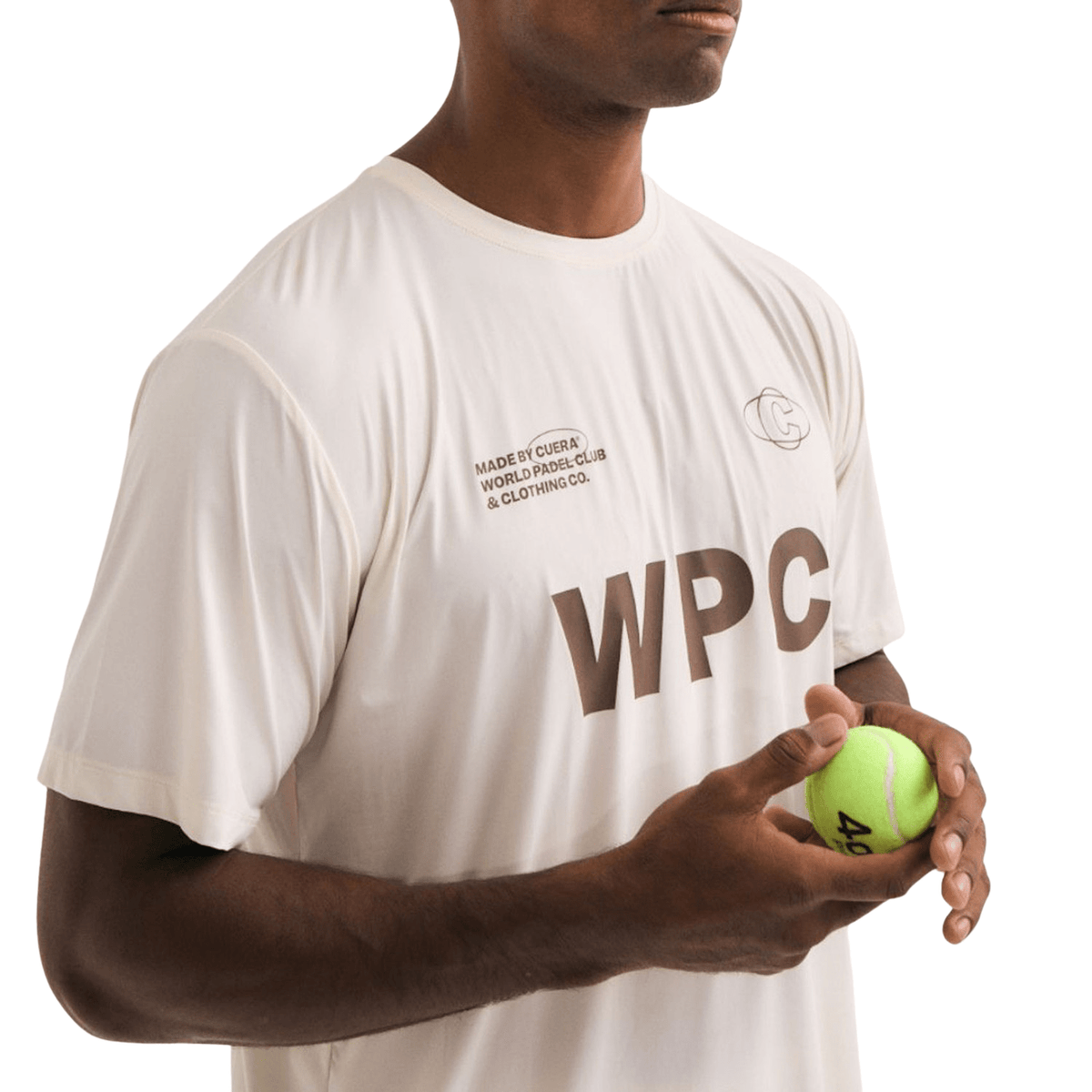 Model in het gebroken witte Cuera WPC T-shirt houdt een padelbal in zijn hand