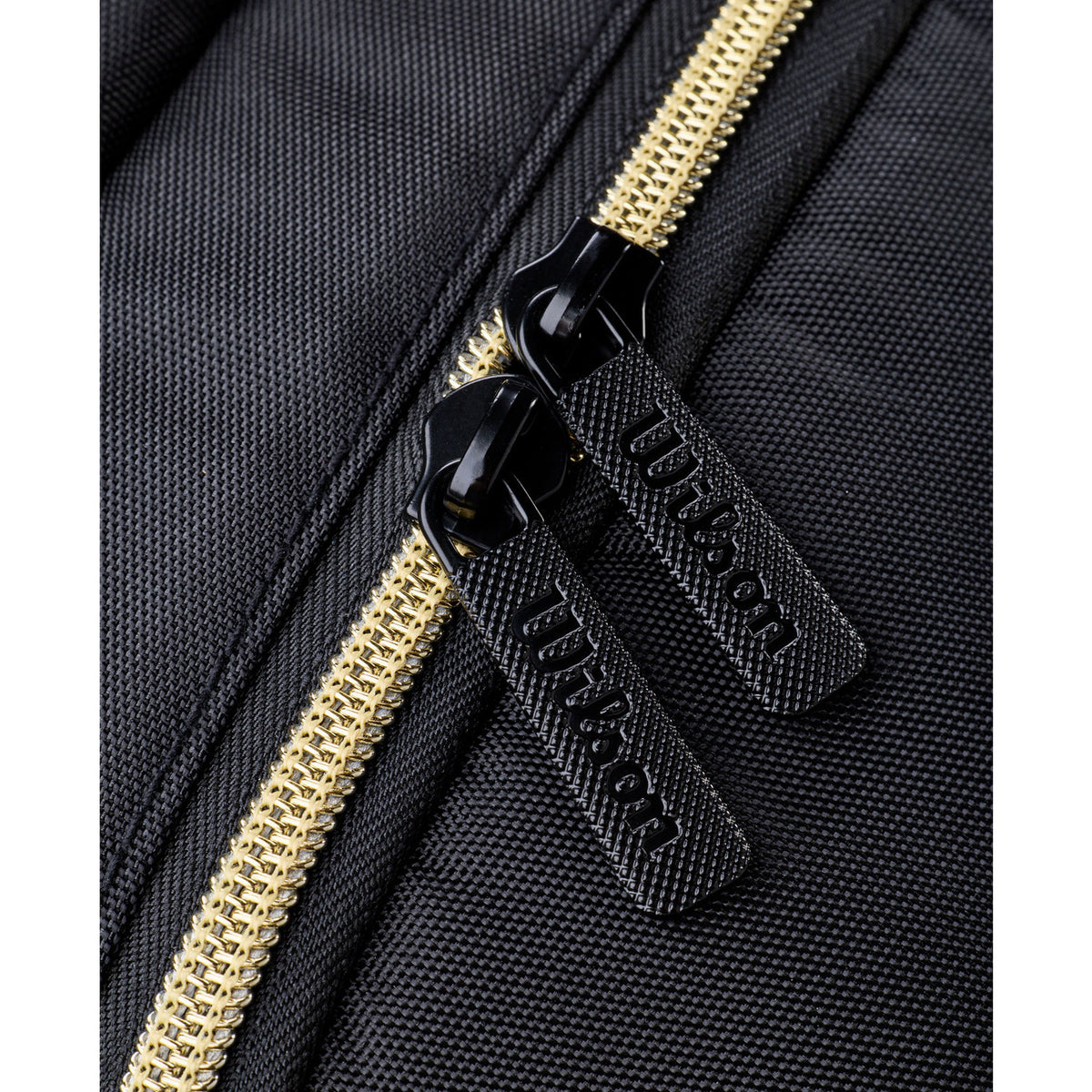 Détail de la fermeture éclair dorée avec tirettes Wilson sur le sac à dos noir