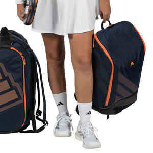 Model met twee donkerblauwe Adidas Protour 2026 rugzakken, een in de hand en een op de rug.