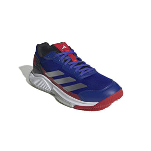 Schuin vooraanzicht van de blauwe Adidas Courtquick met rode hiel