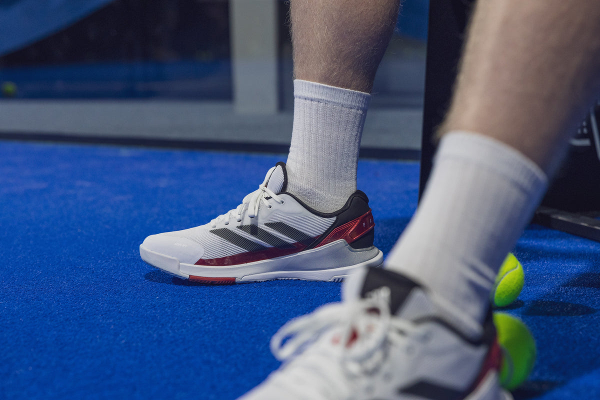 Speler op een blauwe padelbaan draagt witte Adidas Crazyquick LS padelschoenen