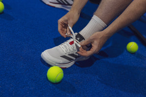 Speler strikt de veters van een witte Adidas Crazyquick LS op de padelbaan