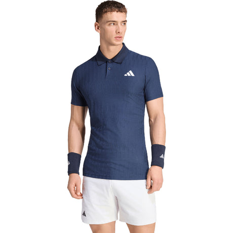 Model draagt de Adidas Freelift polo voor heren in donkerblauw met witte short