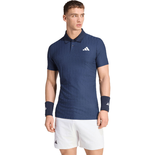 Model draagt de Adidas Freelift polo voor heren in donkerblauw met witte short