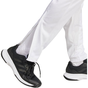 Detail van de enkel van de witte Adidas 3-Stripes broek boven zwarte schoenen