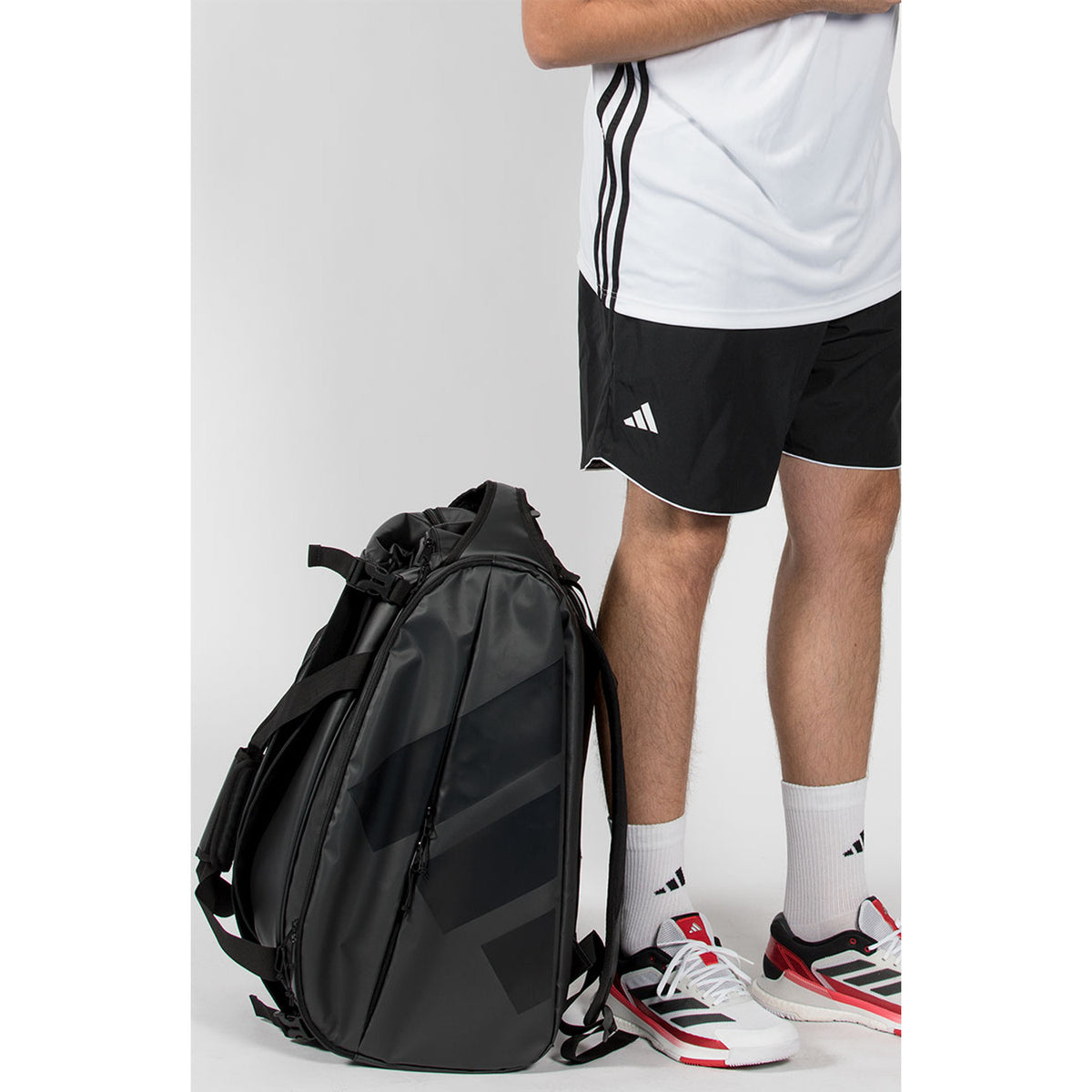 De zwarte Adidas Multigame 2026 racketbag staand naast de benen van een speler.