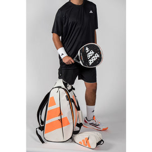 Speler met padelracket naast de creme-oranje Adidas Multigame 2026 racketbag.
