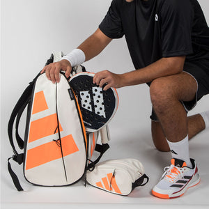 Speler pakt een racket uit de creme Adidas Multigame 2026 racketbag met oranje logo.