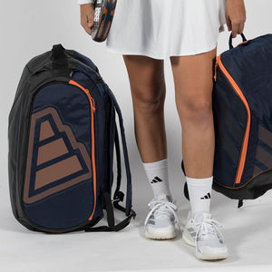 Twee donkerblauwe Adidas Protour 2026 racketbags naast de benen van een speelster.