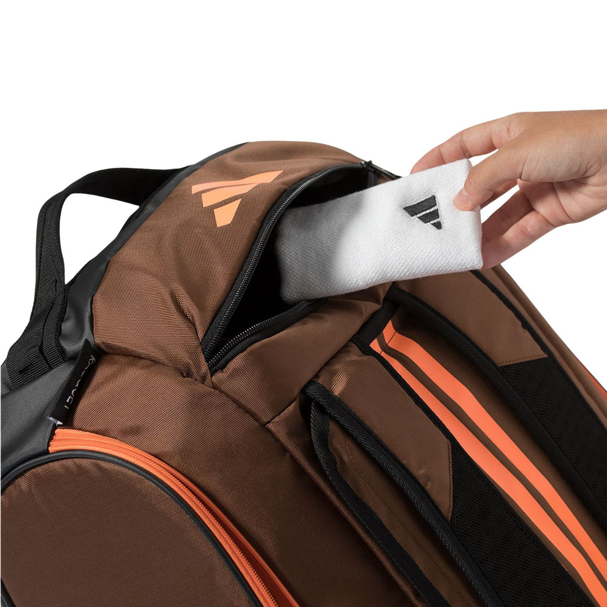 Handdoek wordt in het geopende vak van de bruine Adidas Tour 2026 racketbag gelegd.