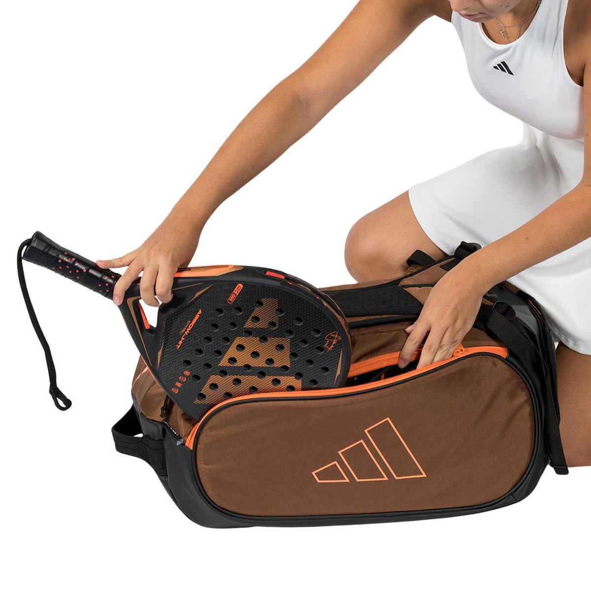Speelster haalt een racket uit de bruine Adidas Tour 2026 racketbag met oranje voering.