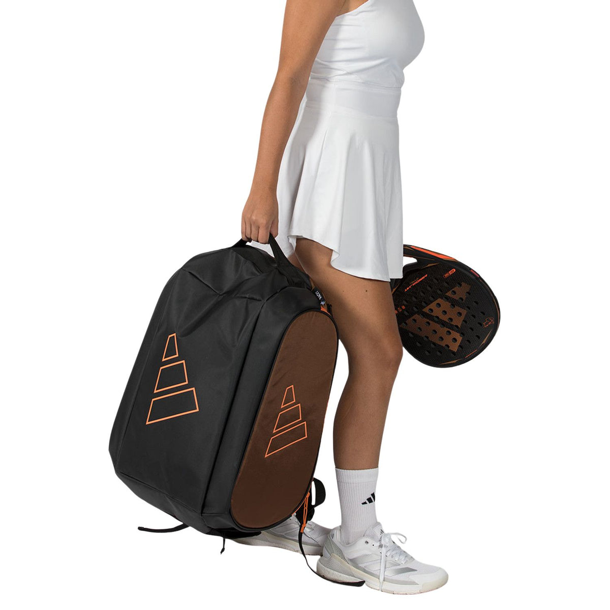 Speelster draagt de donkere Adidas Tour 2026 racketbag aan de hand naast haar racket.