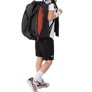 Man draagt de zwart-oranje Adidas Multigame 3.4 racketbag als rugzak met handdoek.