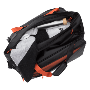 Bovenaanzicht van de geopende zwart-oranje Adidas Multigame 3.4 met handdoek en bidon.