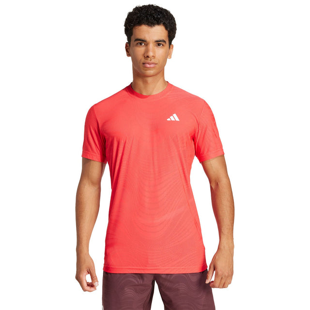 Vooraanzicht van model in het koraalrode Adidas Freelift Pro T-shirt en bordeaux short
