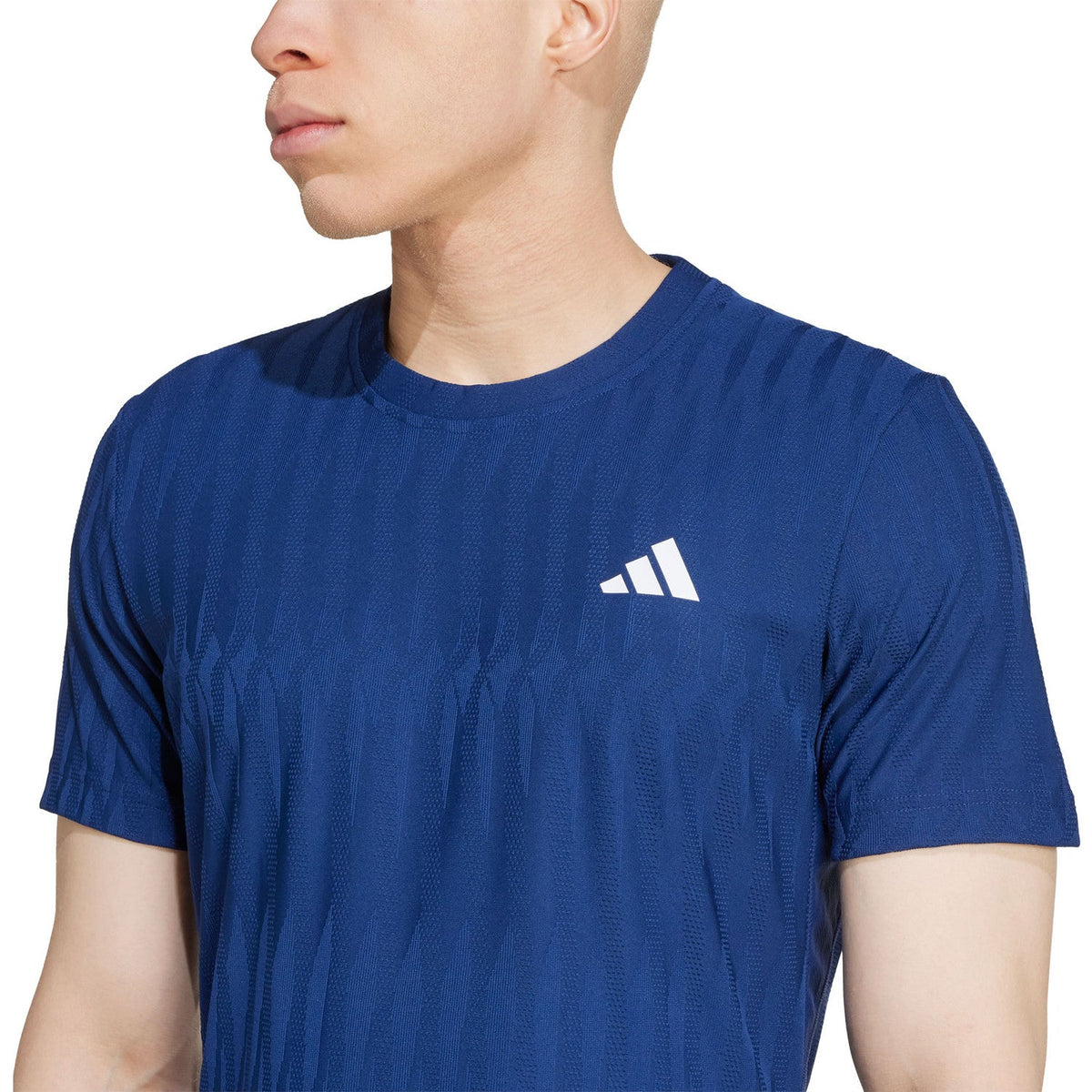 Close-up van het witte borstlogo op het kobaltblauwe Adidas Freelift T-shirt