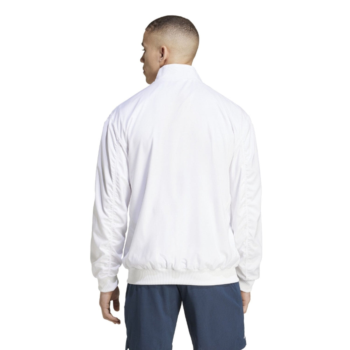 Achteraanzicht van model in het witte Adidas Walk On jack met donkerblauwe broek