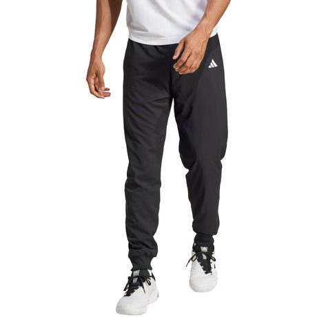 Model draagt de zwarte Adidas Walk On trainingsbroek met wit shirt en witte sneakers, vooraanzicht