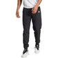 Model draagt de zwarte Adidas Walk On trainingsbroek met wit shirt en witte sneakers, vooraanzicht