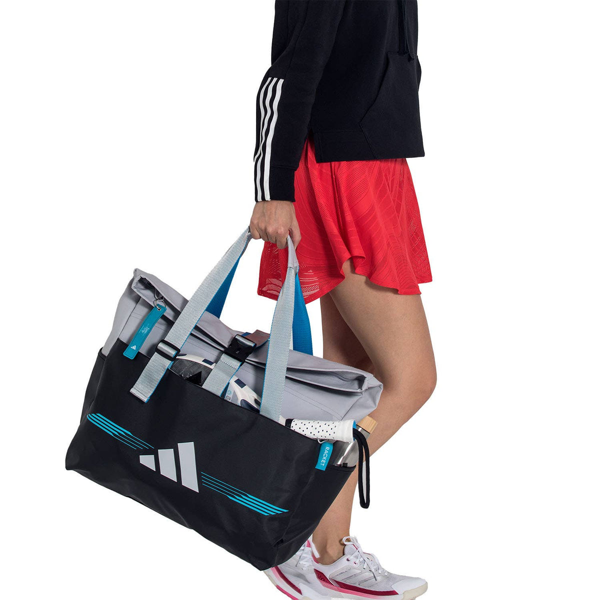 Model draagt de grijs-zwarte Adidas Weekendbag 3.4 in de hand naast een rode rok.