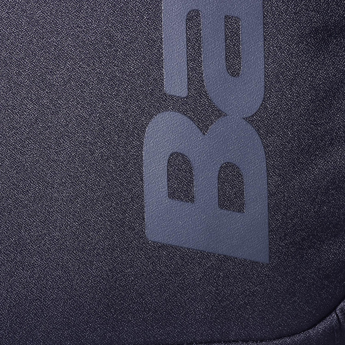 Close-up van het grijze Babolat logo op het zwarte weefsel van de Court Lite rugzak.