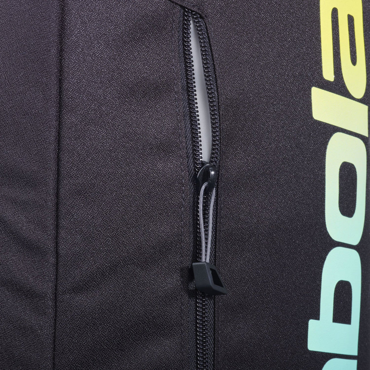 Detail van de rits van de zwarte Babolat Court Lite met geelgroene merknaam.