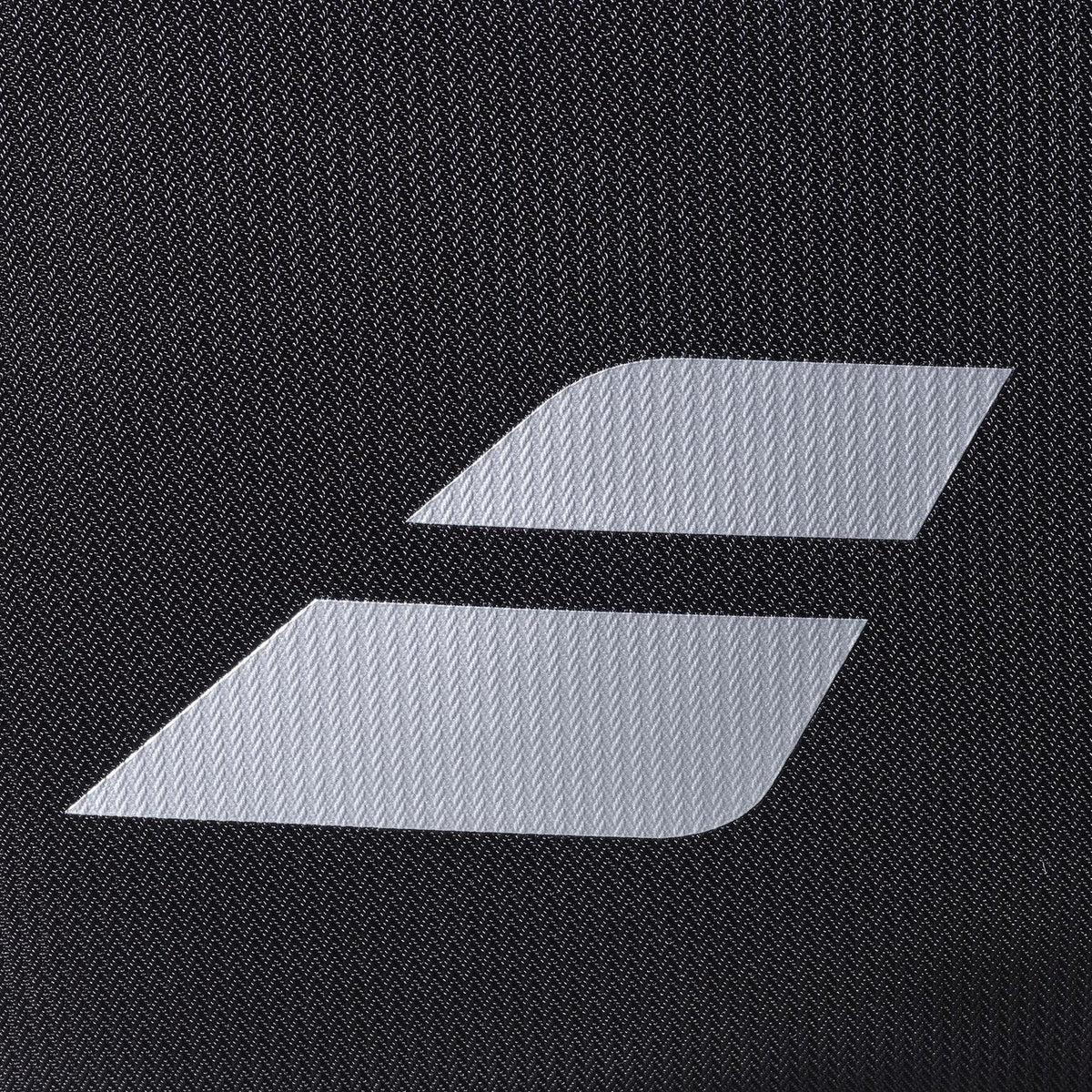 Close-up van het witte Babolat logo op het zwarte weefsel van de RH Perf tas.