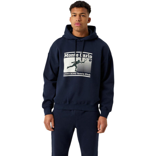 Herenmodel draagt de donkerblauwe Bjorn Borg Oversized Hoodie met Monte Carlo print