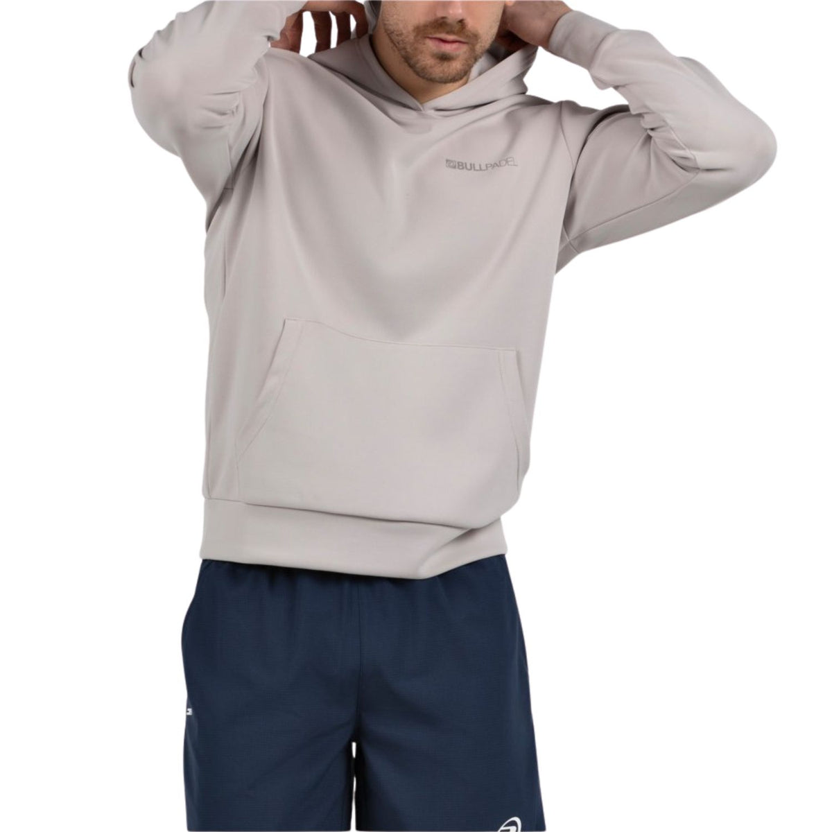 Model trekt de capuchon van de beigegrijze Bullpadel Albier hoodie omhoog