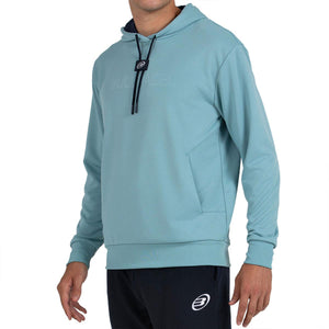 Schuin vooraanzicht van de aquablauwe Bullpadel Hoodie Binee met logo op de borst