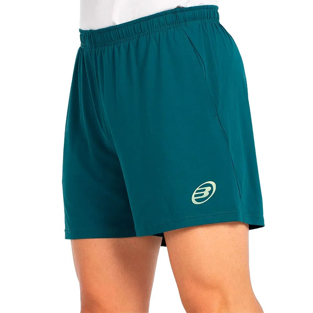 Model draagt de petrolgroene Bullpadel Short Lijar met wit Bullpadel-logo op de pijp
